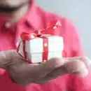 a man holding a white gift box with a red ribbon