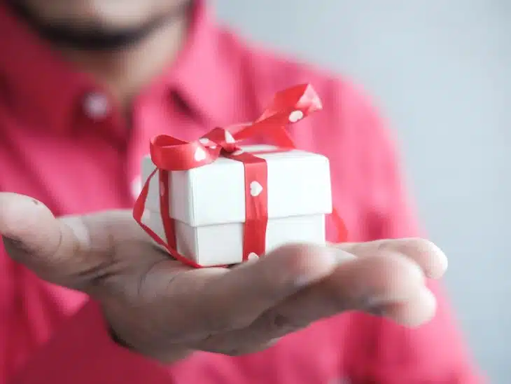 a man holding a white gift box with a red ribbon